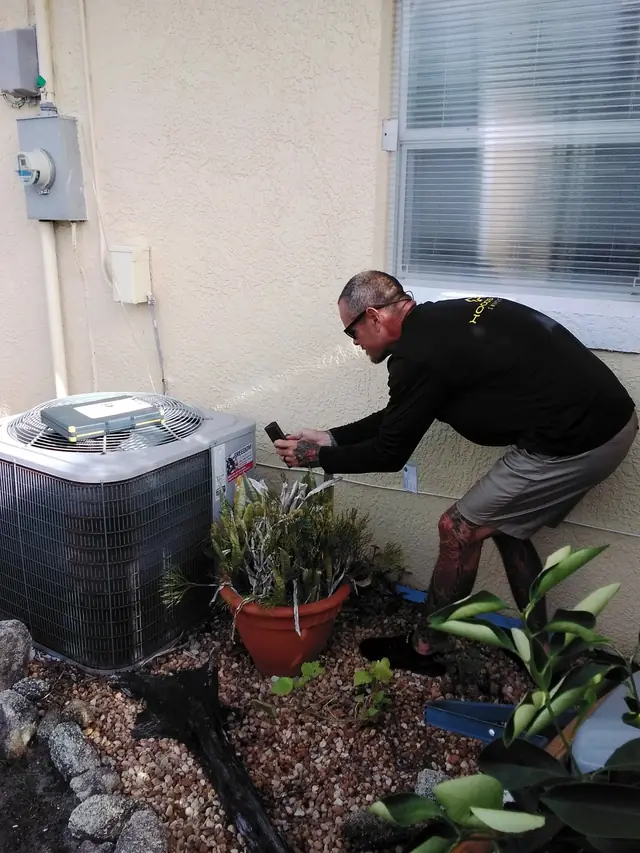Inspector photographing an outdoor air-conditioning condenser against a stucco wall