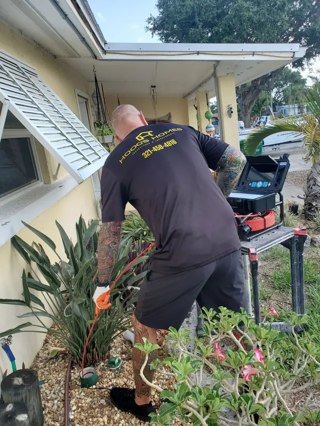 Inspector feeding a sewer-scope camera cable from its reel beside a house